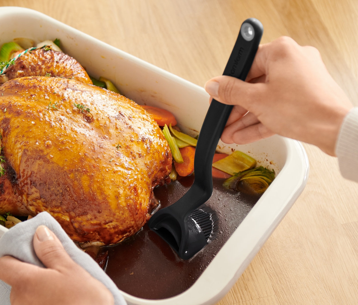 Des mains badigeonnent un poulet rôti dans un plat de cuisson avec un pinceau à cuisson et à rôtissage.