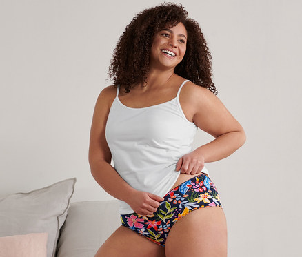 Femme agenouillée sur un lit tenant un caraco blanc et 5 culottes.