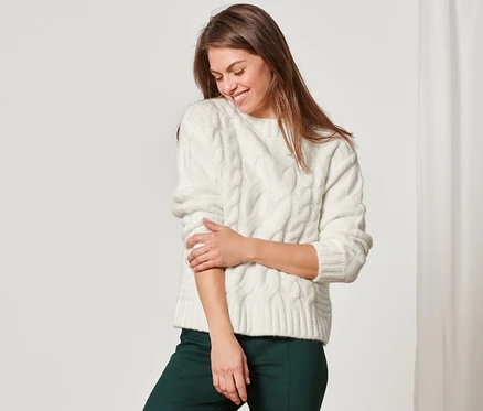 Femme portant un pull en maille avec torsades et un pantalon vert.