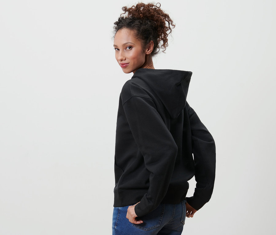Une femme regarde par-dessus son épaule et porte un sweat à capuche noir et un jean.
