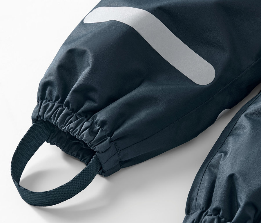 Détail d'un pantalon de pluie pour enfant avec réflecteur et ourlet élastique.