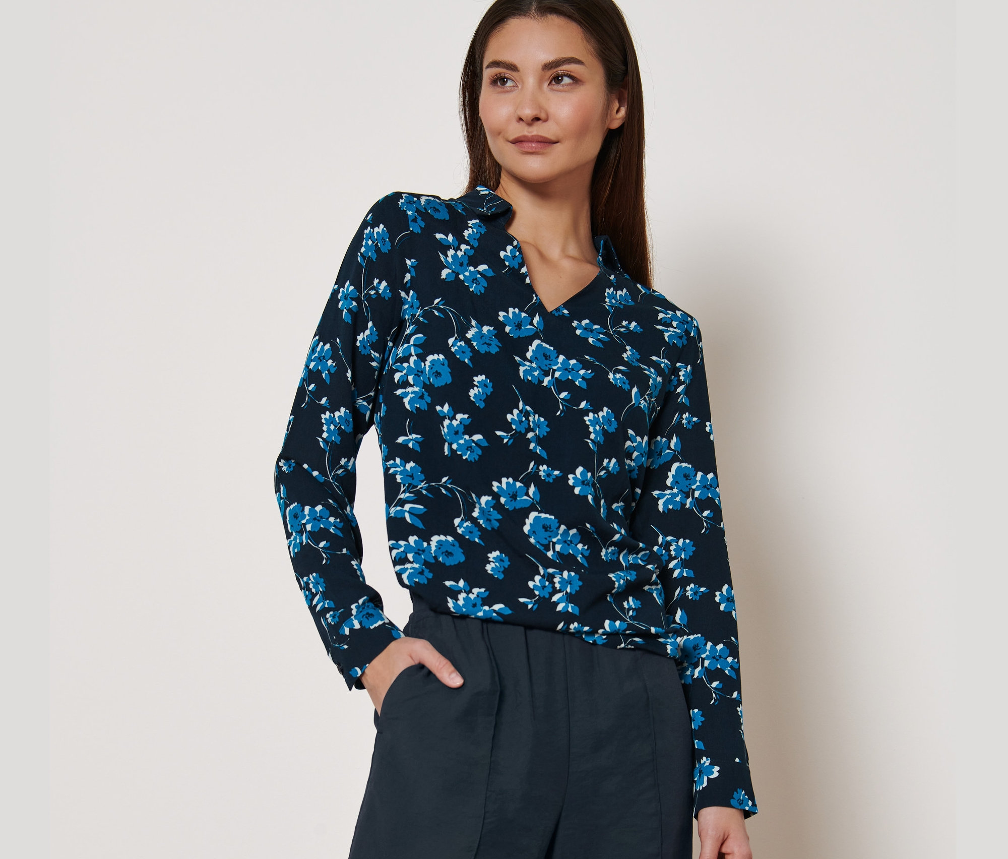 Une femme porte une blouse à imprimé intégral et un pantalon foncé.