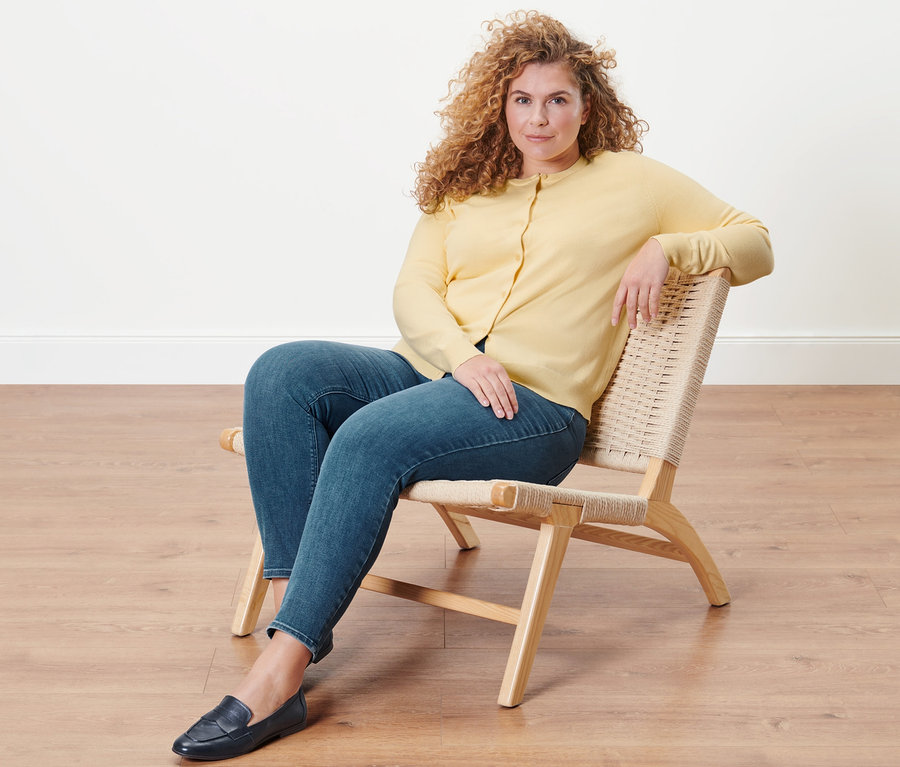 Femme assise dans un fauteuil portant un tregging «
Fit Nelly
» et un cardigan en maille fine.