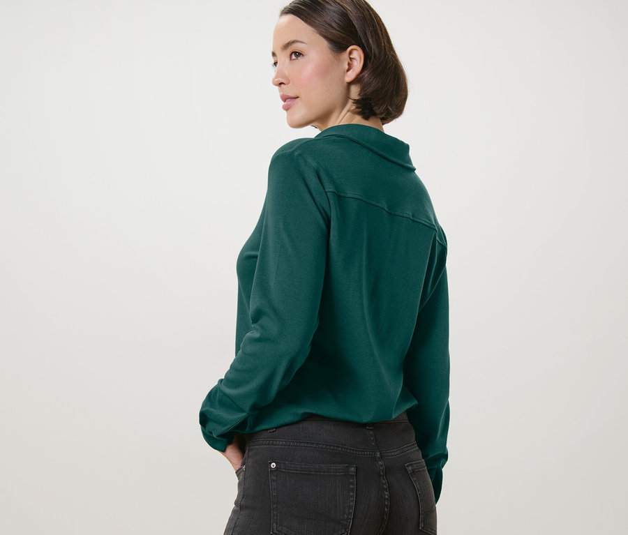 Femme posant en blouse verte avec patte de boutonnage et jean foncé.