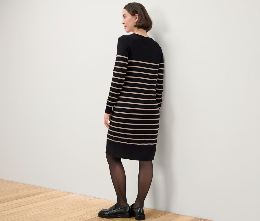 Une femme se tient de côté et porte une robe en maille fine rayée.