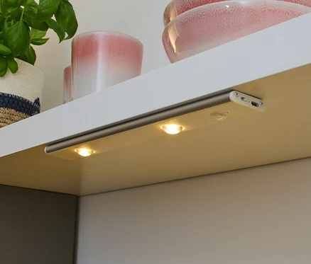 Une lampe multifonctions LED à batterie est fixée sous une étagère et éclaire un plan de travail.