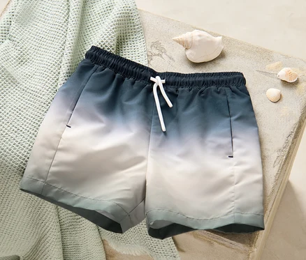 Un boardshort pour enfant posé sur une serviette pliée à côté de coquillages.