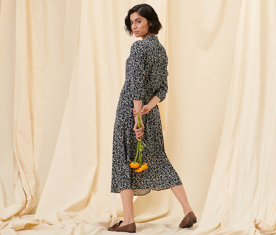 Une femme pose dans une robe-chemisier à motif floral et des loafers en cuir velours.