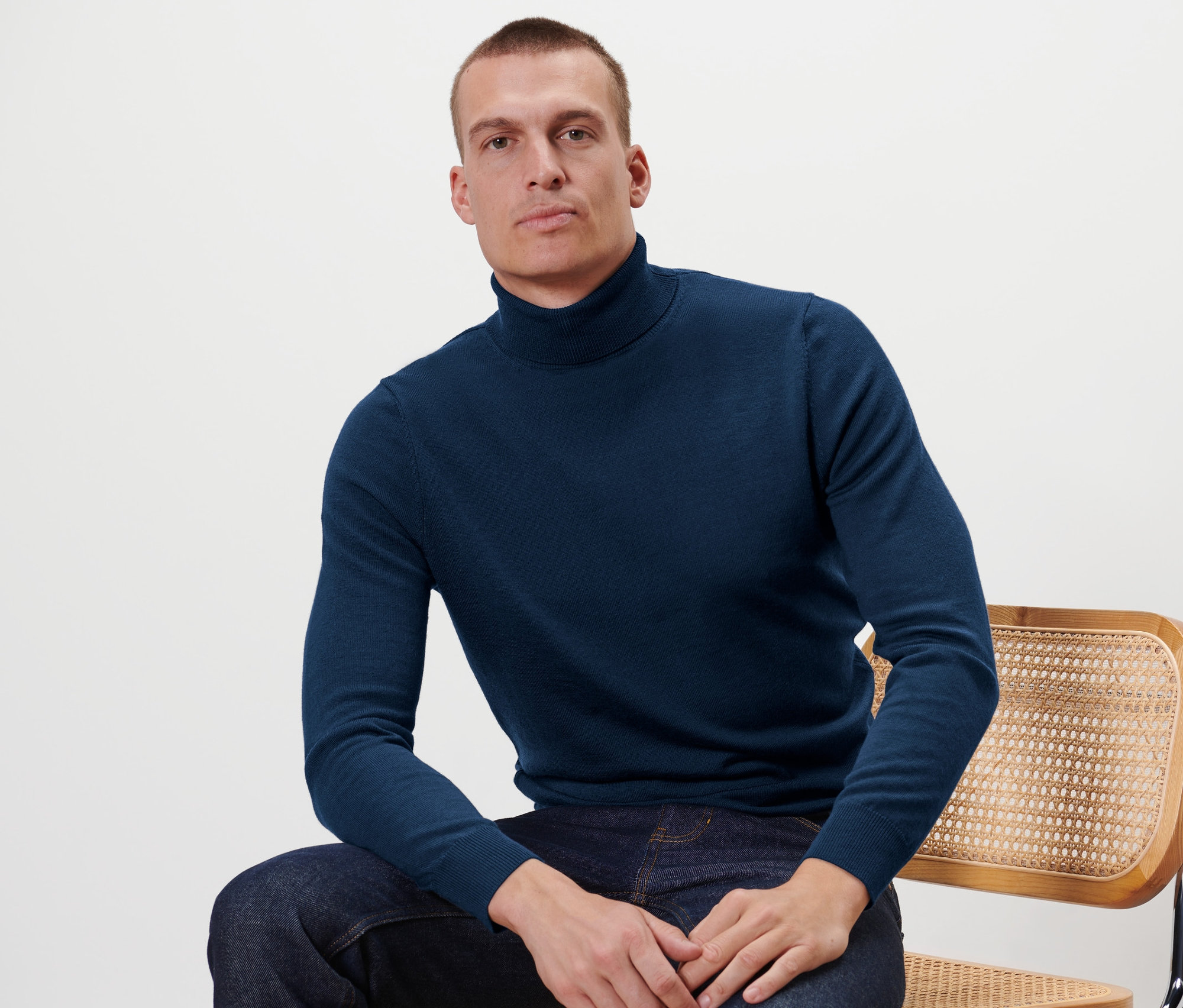Un homme est assis sur une chaise et porte un pull en mérinos bleu marine.