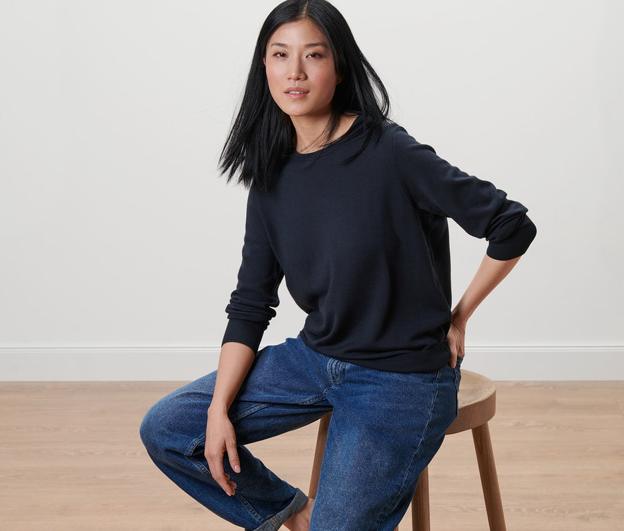 Une femme est assise sur un tabouret et porte un pull en maille fine de mérinos bleu foncé.