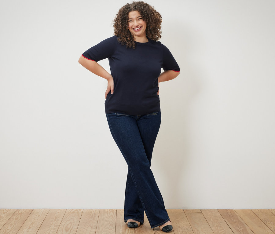 Femme posant dans un pull en maille fine bleu foncé et un jean flare – Fit «  Cara ».