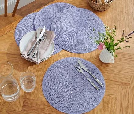 Quatre sets de table violets sur une table en bois avec des assiettes, des couverts, des verres et un vase avec des fleurs.