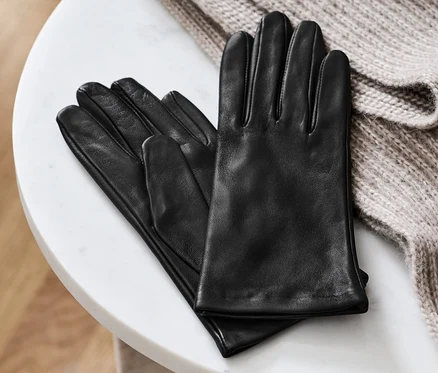 Des gants en cuir noirs reposent sur une table en marbre blanc à côté d'un pull en tricot beige.