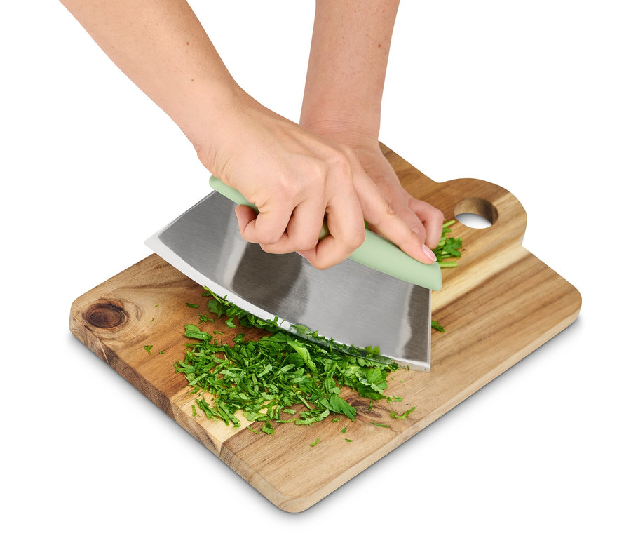 Des mains coupent des herbes avec une trancheuse pour herbes et pizza sur une planche à découper.
