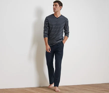 Un homme debout portant un pyjama. Il se compose d'un haut rayé à manches longues et d'un pantalon bleu marine.