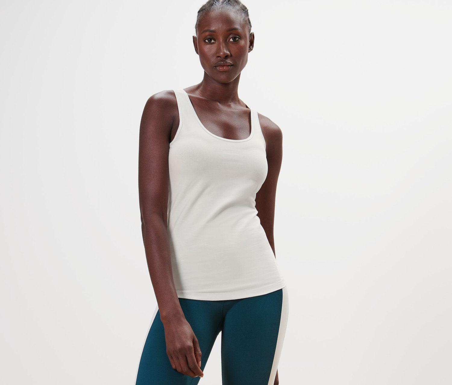 Une femme à la peau foncée est debout et porte un haut blanc cassé et un legging vert.