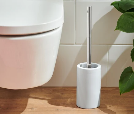 Une cuvette de toilette et une brosse de toilette blanche posées sur un plancher en bois à côté d'un tapis rose.