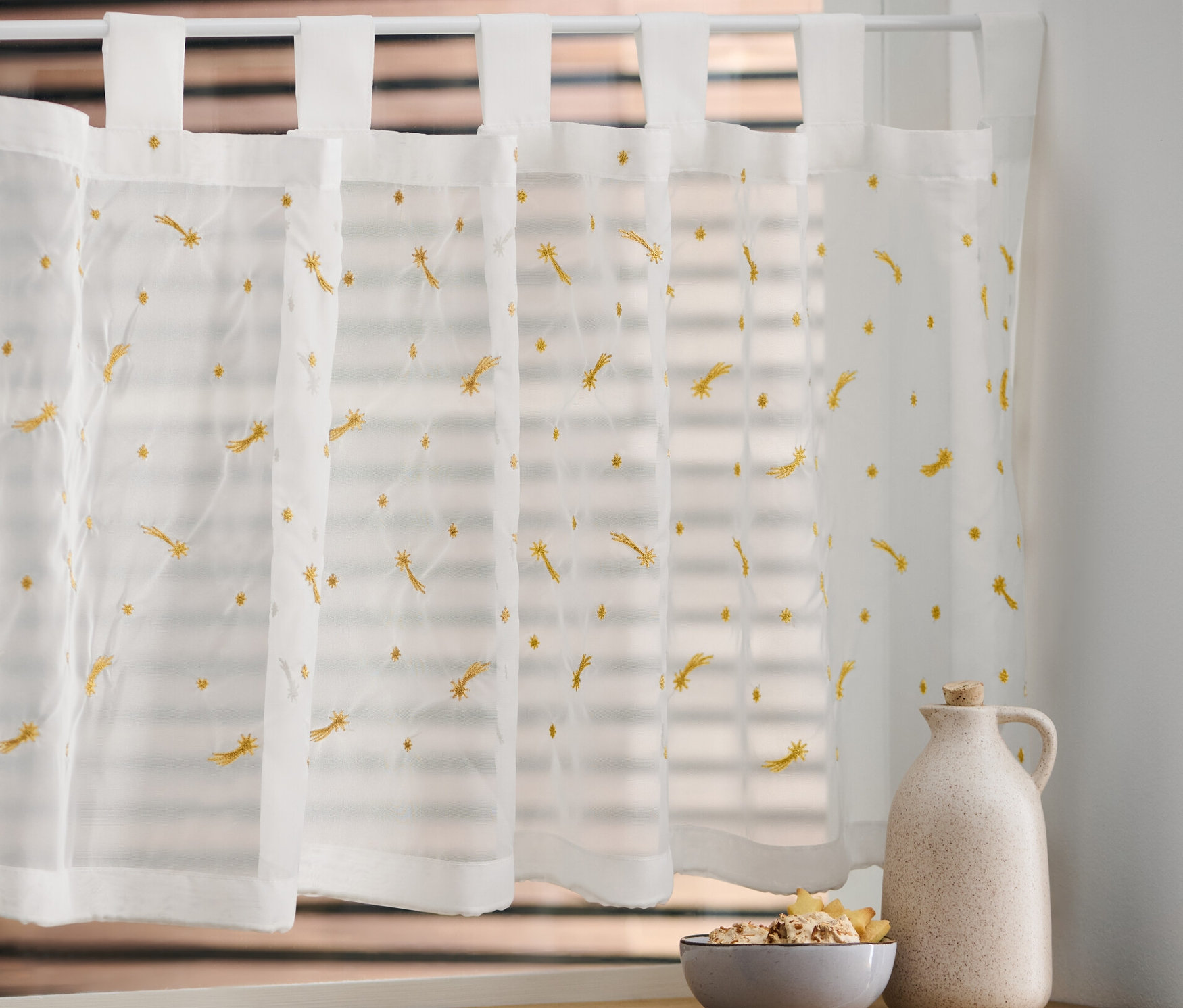 Rideaux bistrot brodés sur une fenêtre.