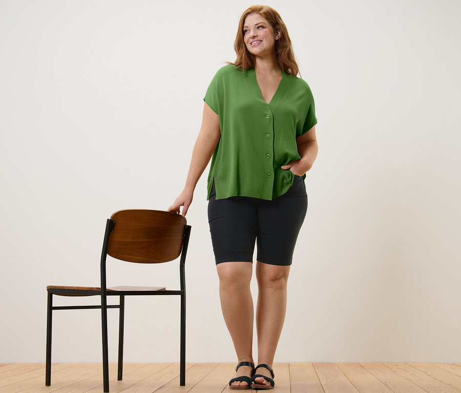 Femme posant en cardigan vert à manches courtes et bermuda en bengaline noir.