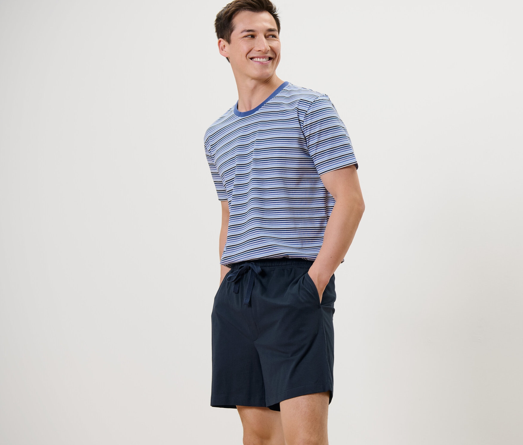 Un homme debout souriant porte un pyjashort bleu et bleu foncé.