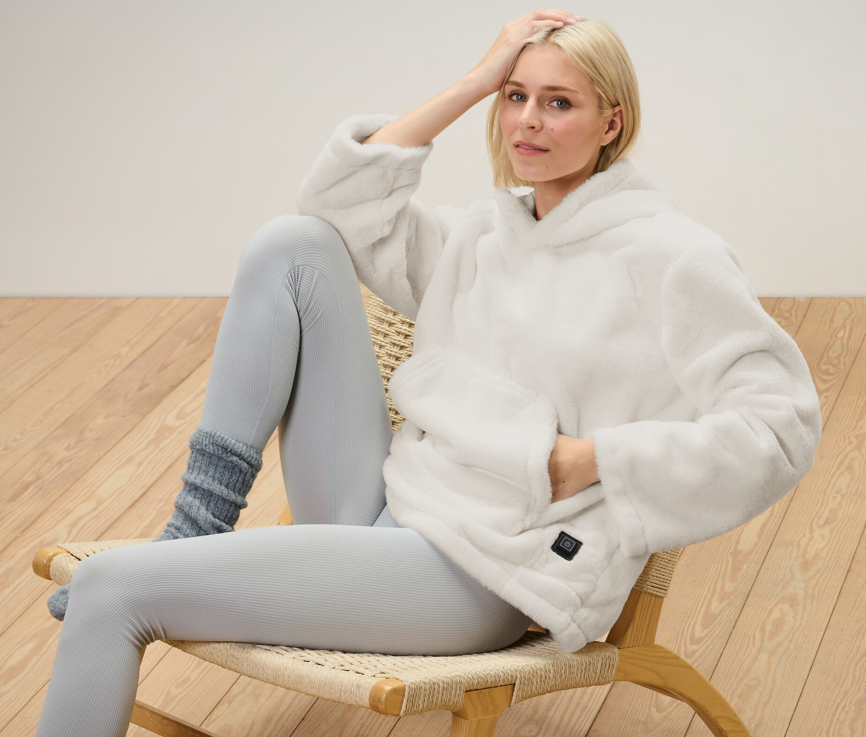 Une femme blonde est assise sur une chaise et porte un pull chauffant à batterie.