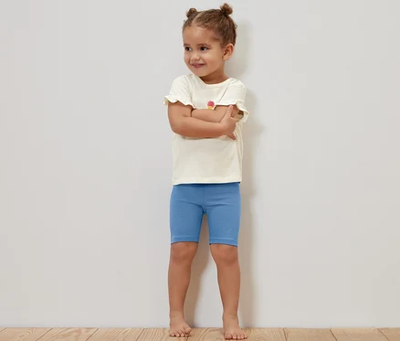 Une fille se tient les bras croisés et porte des leggings de cycliste bleus pour enfants.