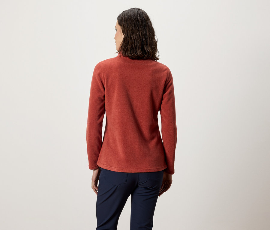 Une femme, dos à la caméra, porte un haut en polaire orange et un pantalon bleu marine.