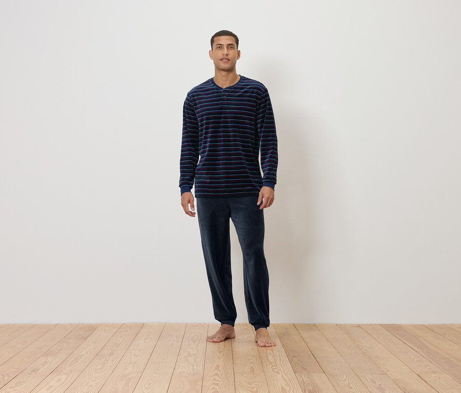 Un homme debout sur un plancher en bois porte un pyjama rayé bleu marine.