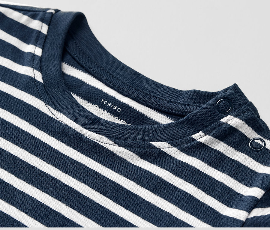 Gros plan sur un t-shirt à manches longues pour enfant rayé bleu et blanc avec des boutons sur l'épaule.