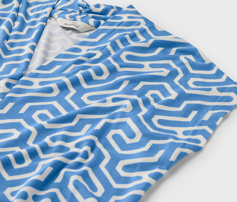 Gros plan sur une blouse bleue à encolure en V avec un motif géométrique blanc.
