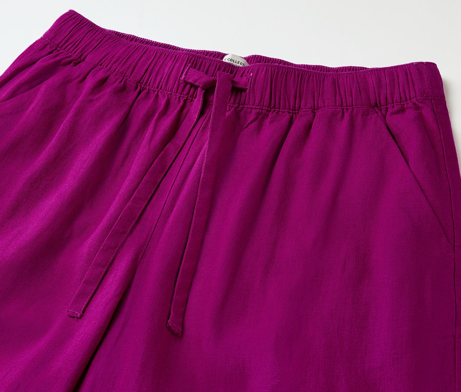 Gros plan d'un pantalon en lin rouge baie avec une taille élastique et un cordon de serrage.