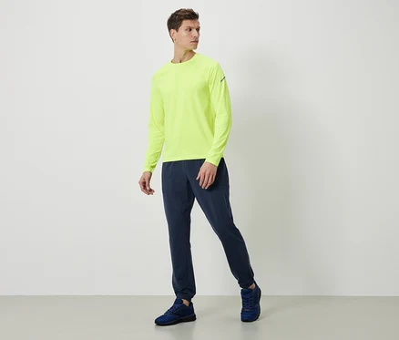 Homme portant un t-shirt à manches longues jaune néon, un pantalon de survêtement bleu marine et des chaussures bleues.