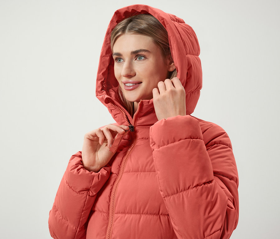 Femme fermant la fermeture éclair d'une doudoune à capuche corail.