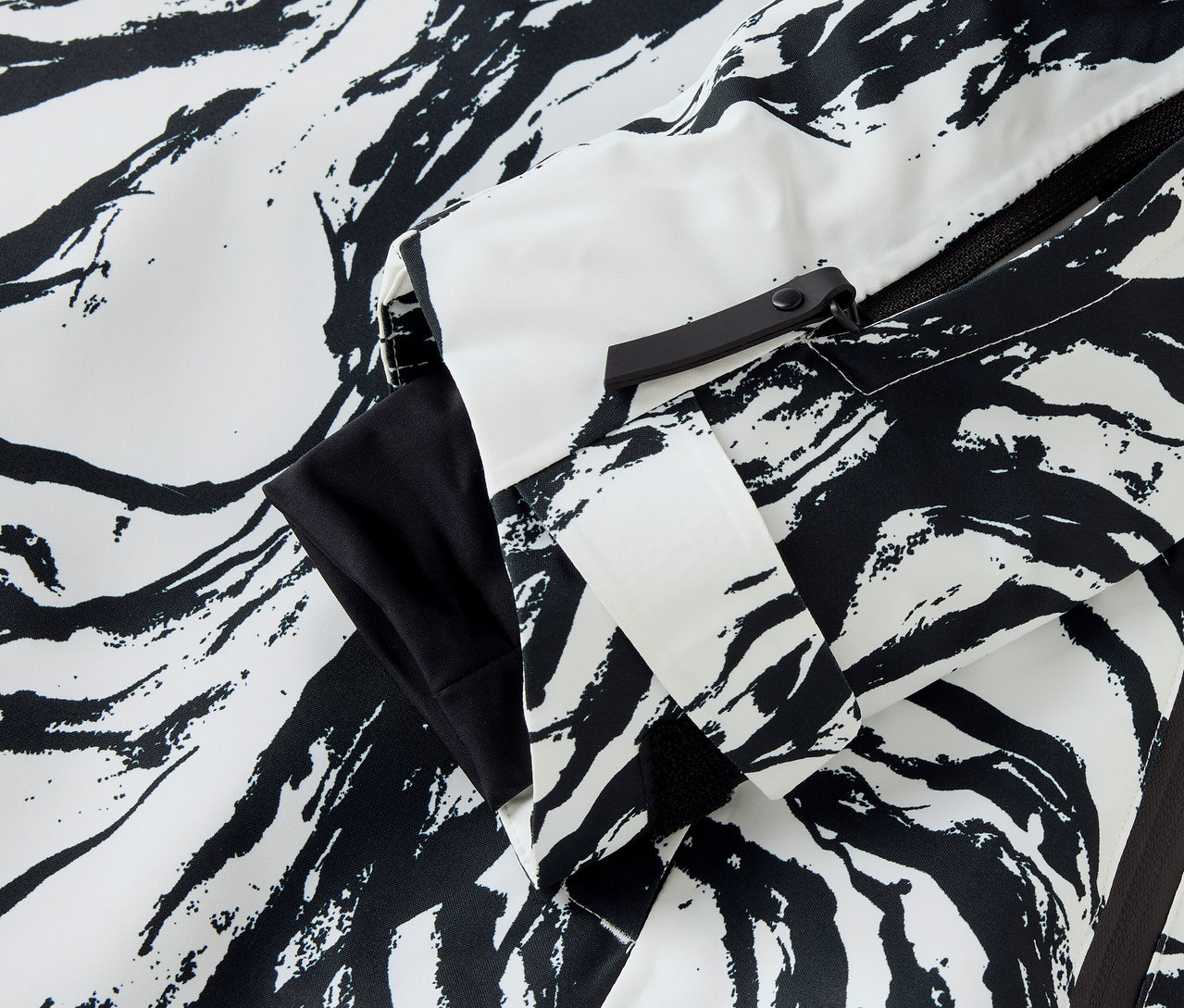 Détail d'une veste à motif zébré en noir et blanc, avec une manche et une fermeture éclair visibles.