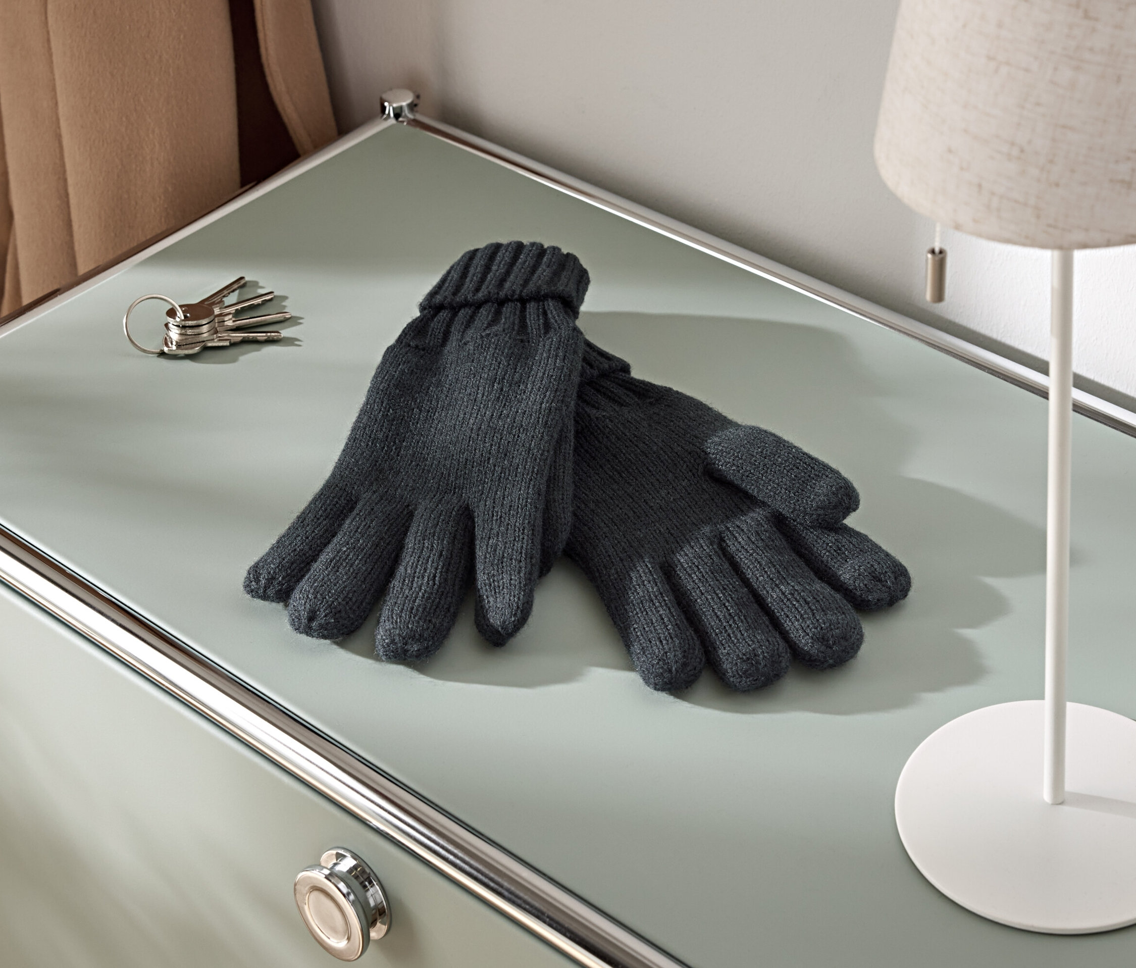 Sur une armoire, il y a une paire de gants tricotés, un trousseau de clés et une lampe.