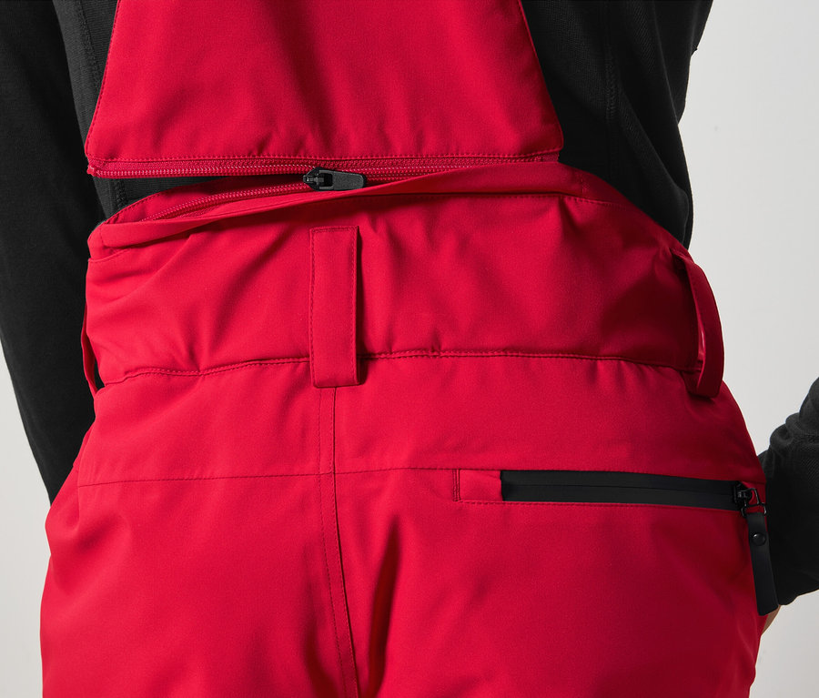 Détail d'un pantalon à bretelles rouge avec fermeture éclair noire.