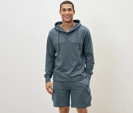 Un homme debout portant un sweat à capuche bleu et un short.