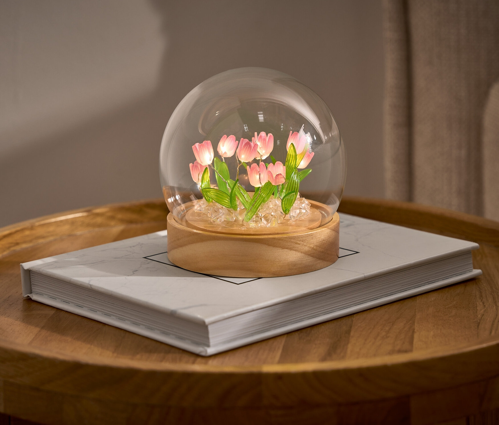 Un LED-DIY-Bastel-Set avec des tulipes dans un dôme en verre sur un livre sur une table ronde.
