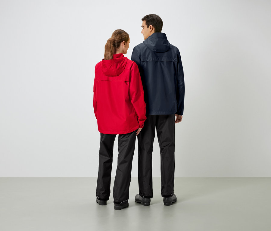 Deux personnes se tiennent dos à la caméra, portant des vestes et des pantalons de pluie.