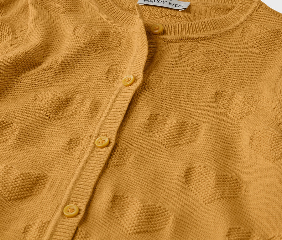 Gros plan sur un veste en maille pour enfant jaune moutarde avec une rangée de boutons et des motifs de cœurs.