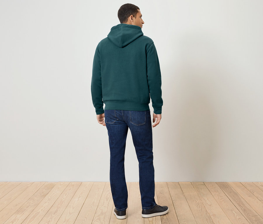 Un homme, vu de dos, porte un sweat à capuche vert foncé, un jean et des baskets.