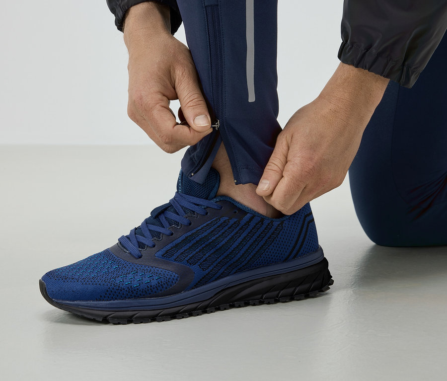 Un homme ferme la fermeture éclair d'un pantalon de course bleu, et porte des chaussures bleues.