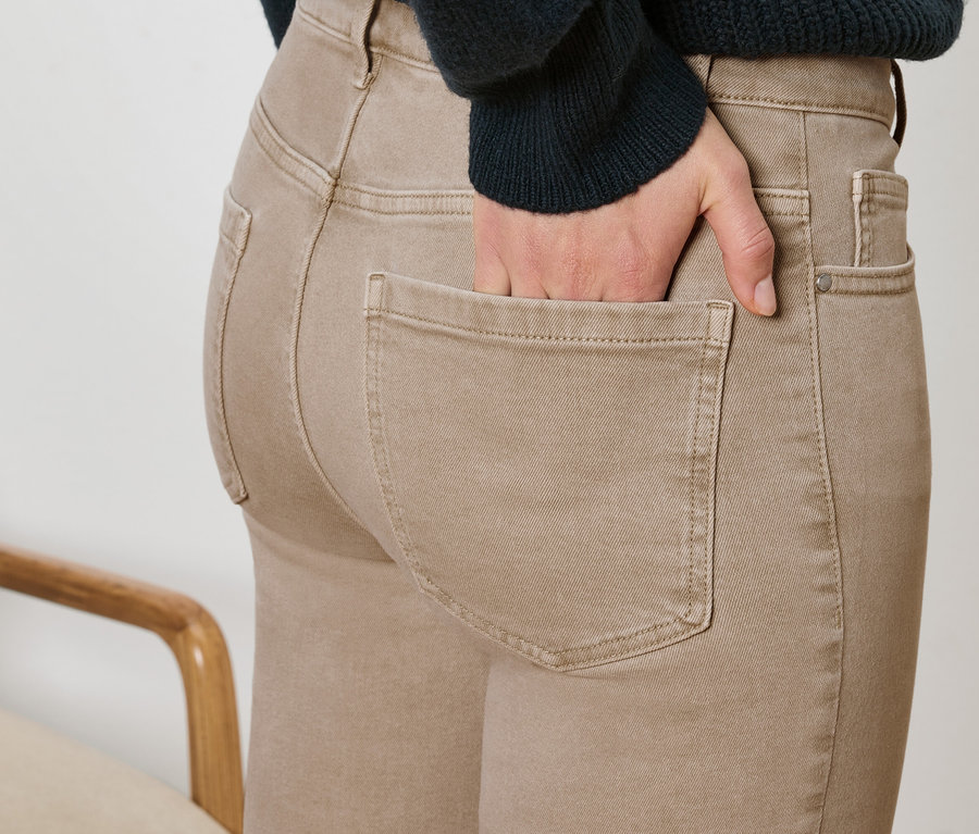 Gros plan d'une femme portant un pantalon marron avec une main dans la poche et un morceau de chaise.