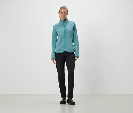 Une femme debout portant une veste en polaire turquoise et un pantalon noir.