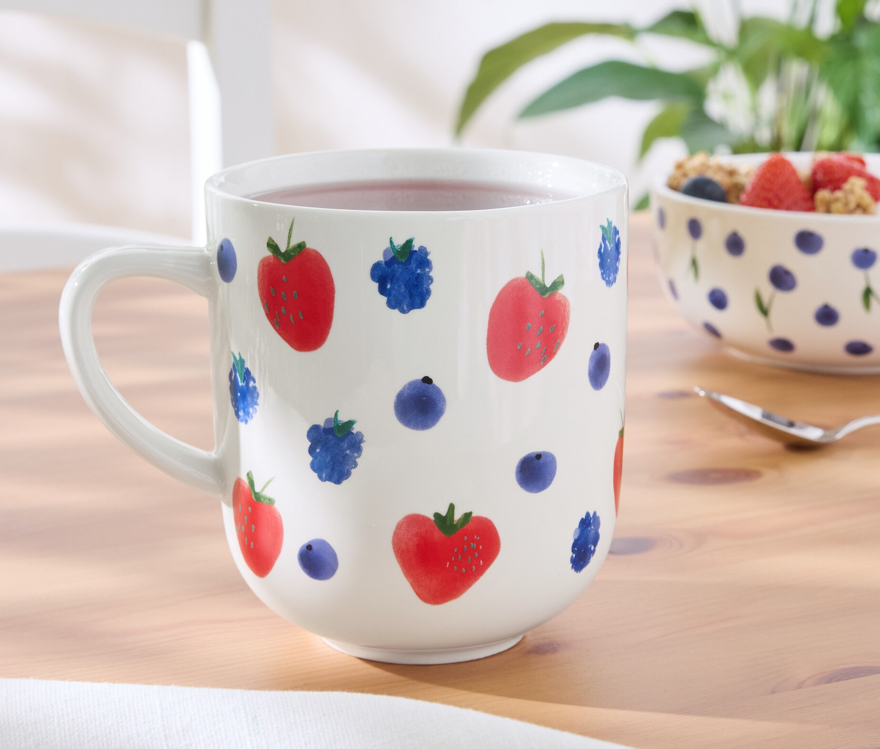 Sur une table, une grand mug avec un motif de fraises et de myrtilles.