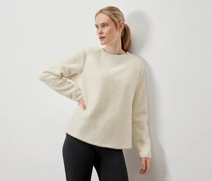Femme posant dans un pull crème et un legging noir.