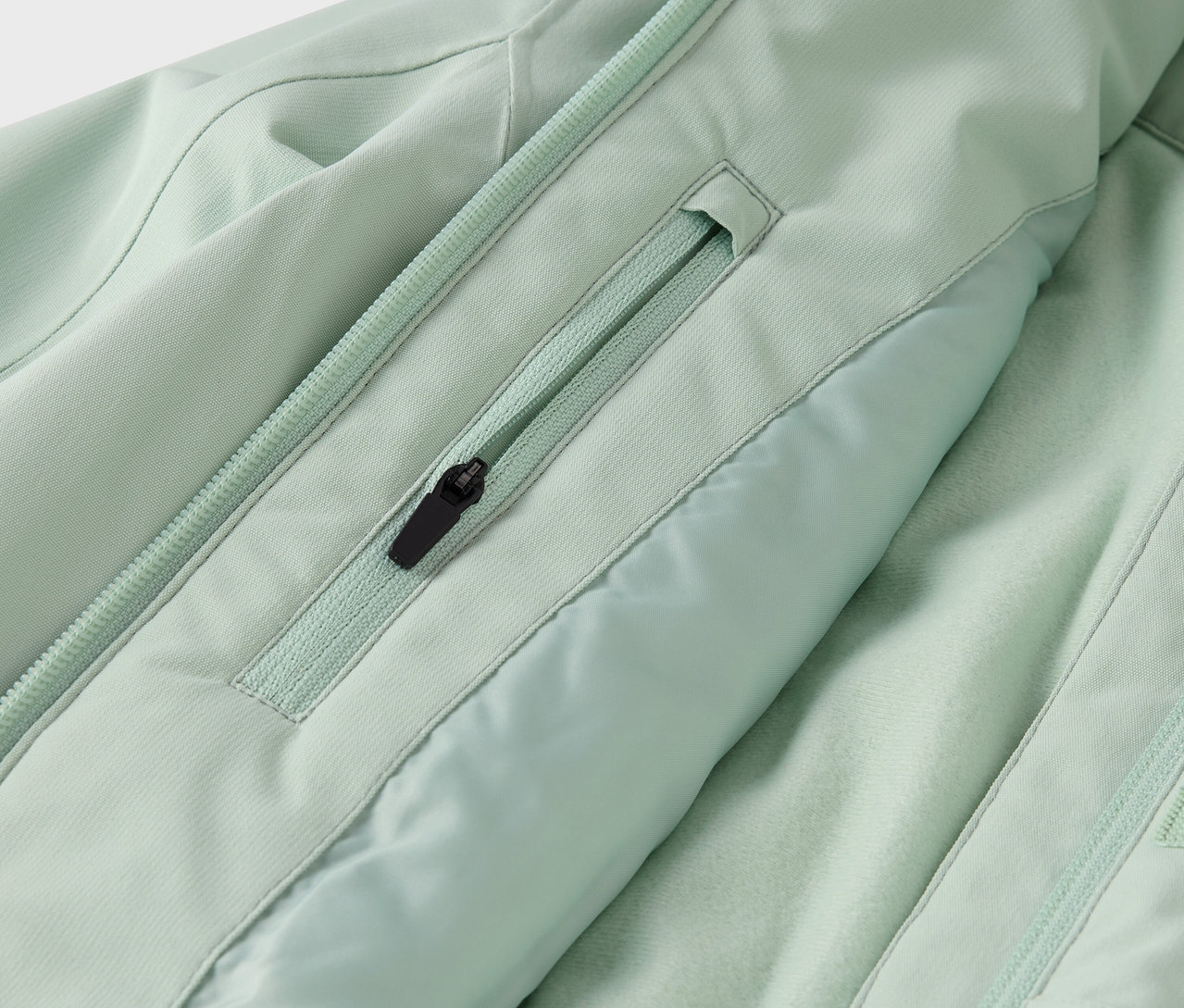 Gros plan sur une veste vert clair avec une poche zippée et une fermeture éclair au centre.