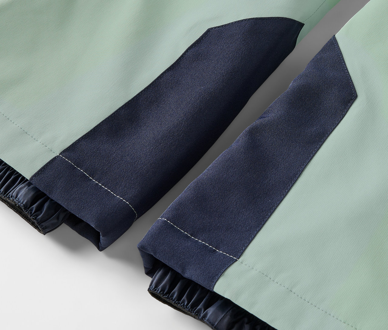 Gros plan sur une veste vert clair avec des manches bleu foncé et des poignets élastiques.