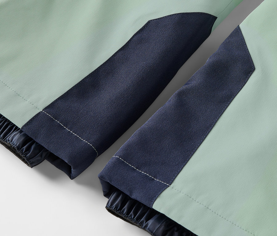 Gros plan sur une veste vert clair avec des manches bleu foncé et des poignets élastiques.