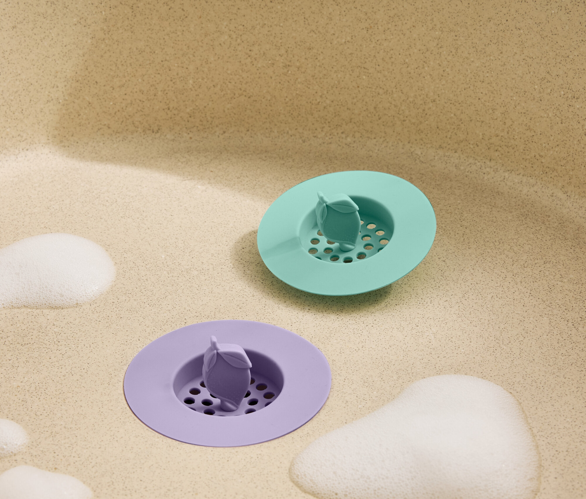 Vue de dessus d'un bouchon d'évier vert et violet avec de la mousse dans un évier beige.